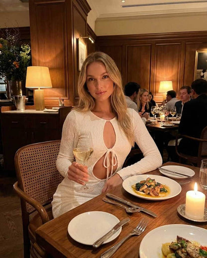 A woman wearing the Serene Maxi Dress by Lauven, elegantly seated at a dining table holding a glass of wine.