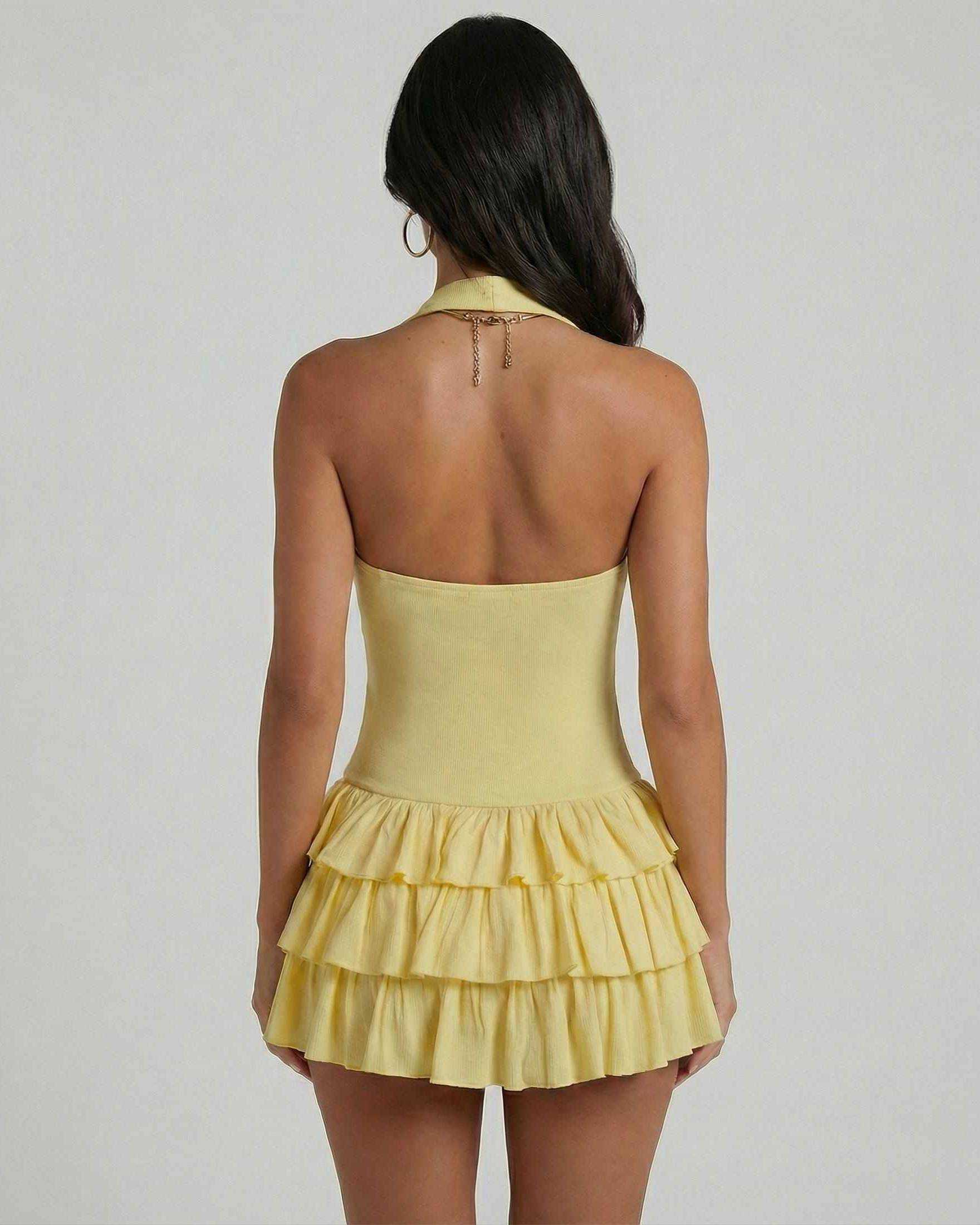 Back view of a woman wearing the Solara Mini Dress by Lauven, featuring a tiered skirt and square neckline in yellow.