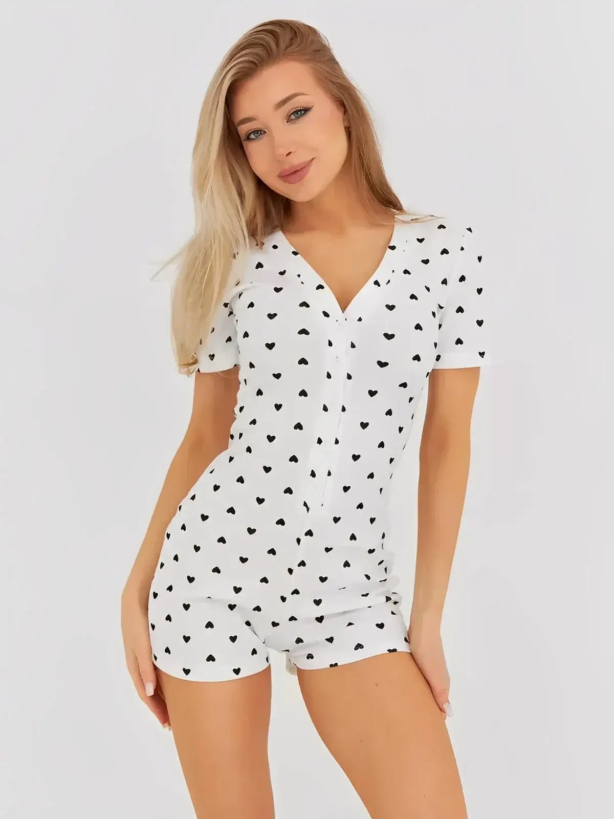 Model wearing Sweetheart Playsuit by Lauven in white with black heart print, featuring a V-neck and button front.