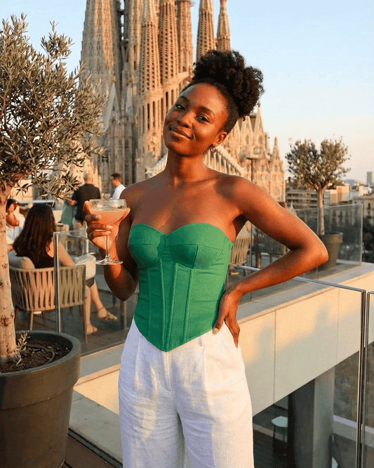 Woman wearing Verde Corset Top by Lauven, holding a cocktail with a city view backdrop.