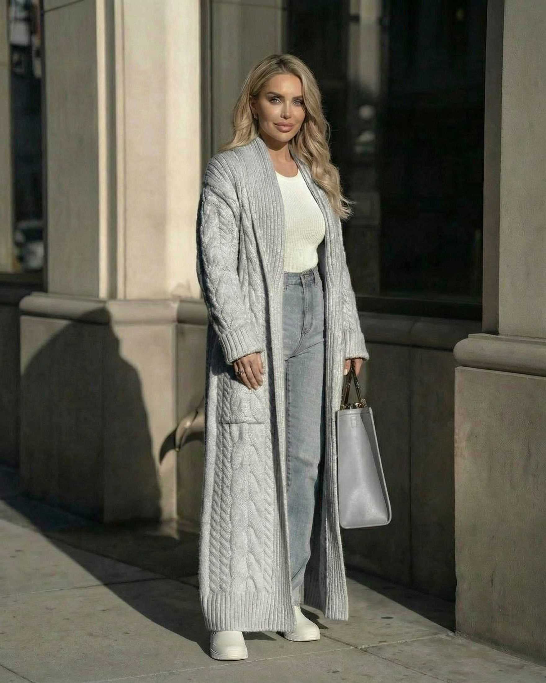 Model wearing the Lauven Verona Cardigan, a long cable-knit wool-blend cardigan in gray, styled with jeans and a bag.