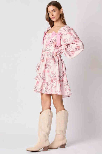 Model wearing the Lila Mini Dress, a floral pink dress with bow accents, paired with stylish knee-high boots.