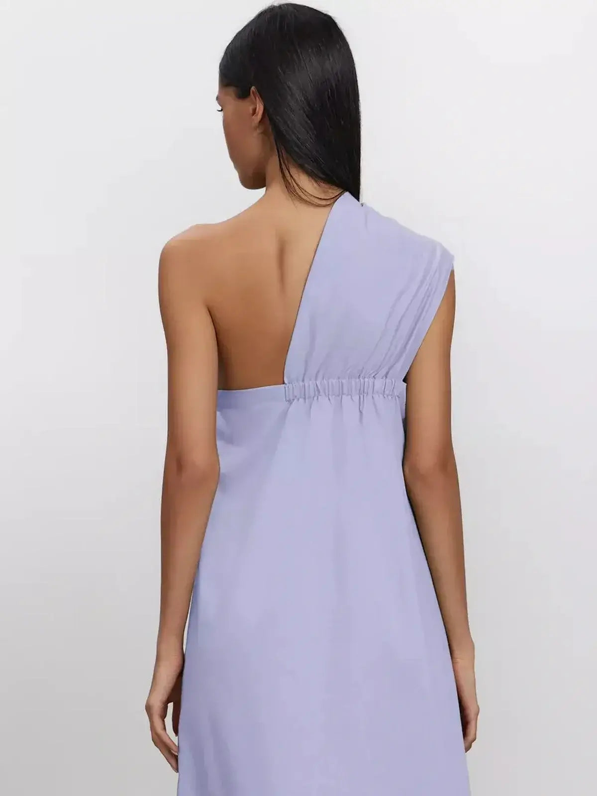 Back view of a woman in a lilac flow maxi dress showcasing its one-shoulder design and soft draping.