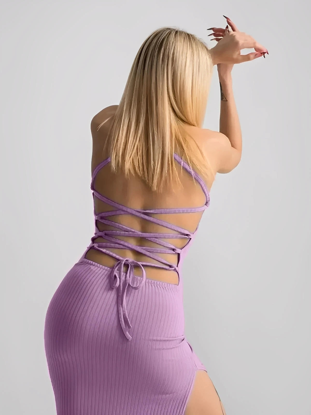 Back view of a model in a lilac lace midi dress showcasing a corset back and high side slit, highlighting a stylish silhouette.