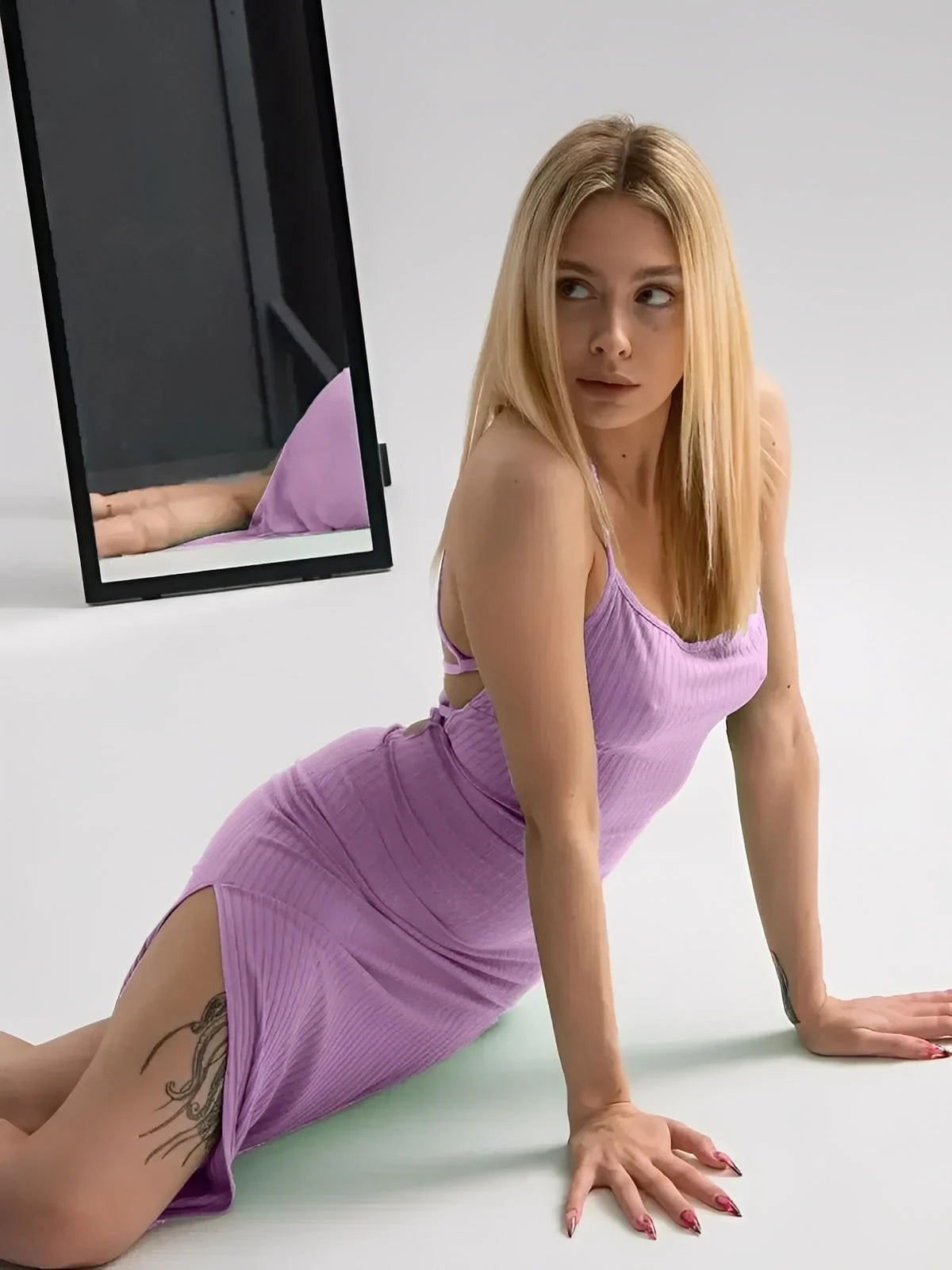 Model wearing a lilac lace midi dress with a ribbed fit, showcasing thin straps and a high side slit against a mirrored background.