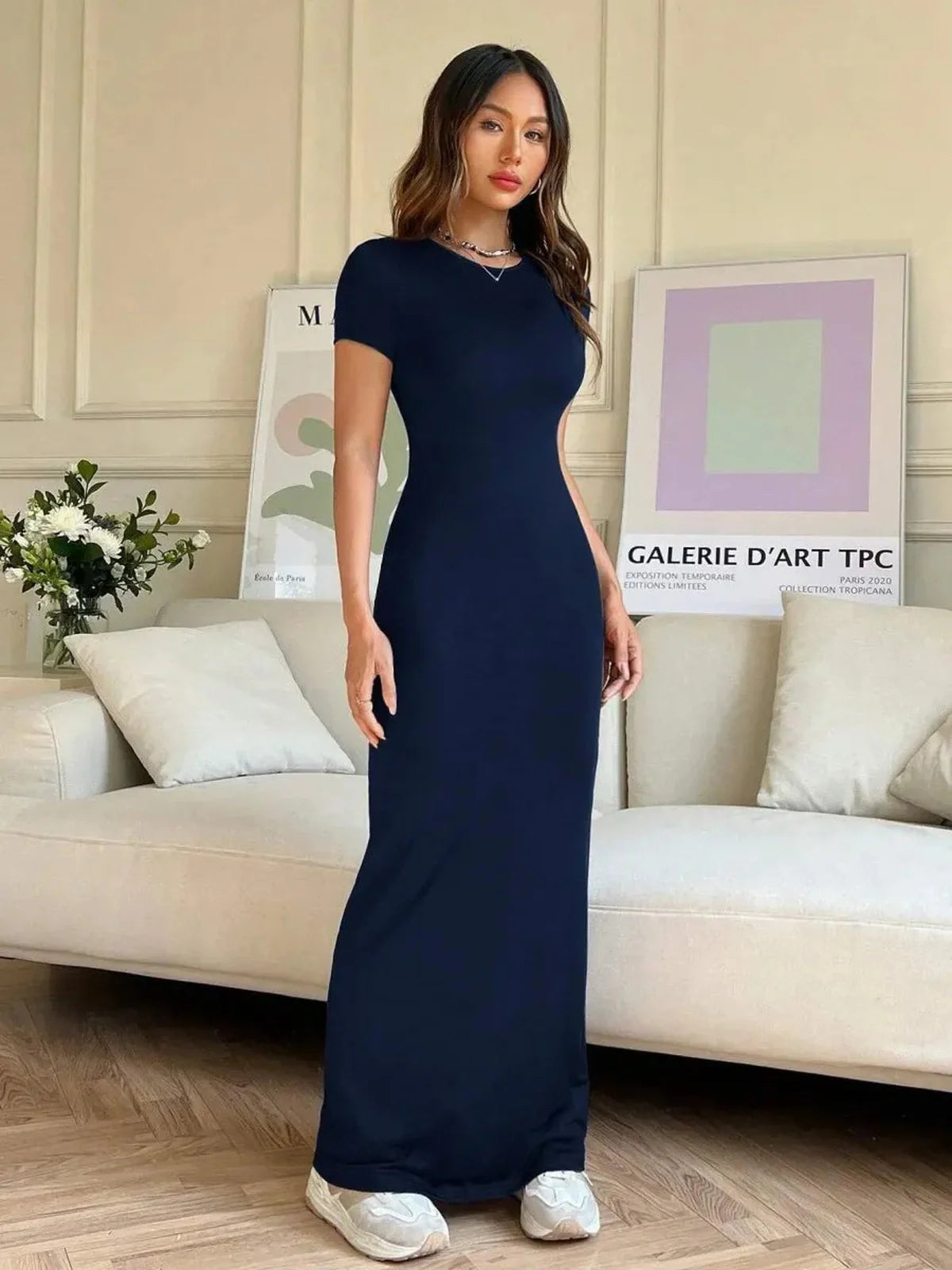 Luna Curve Maxi Dress in navy, featuring a sleek silhouette and asymmetric neckline, styled elegantly in a modern living room.