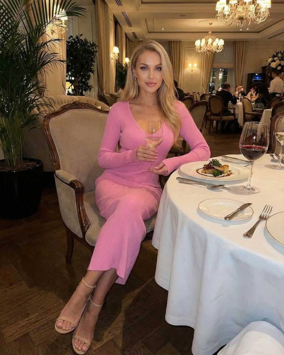Luna Midi Dress by Lauven worn by a woman in a soft pink ribbed v-neck knit dress at an elegant dining setting.