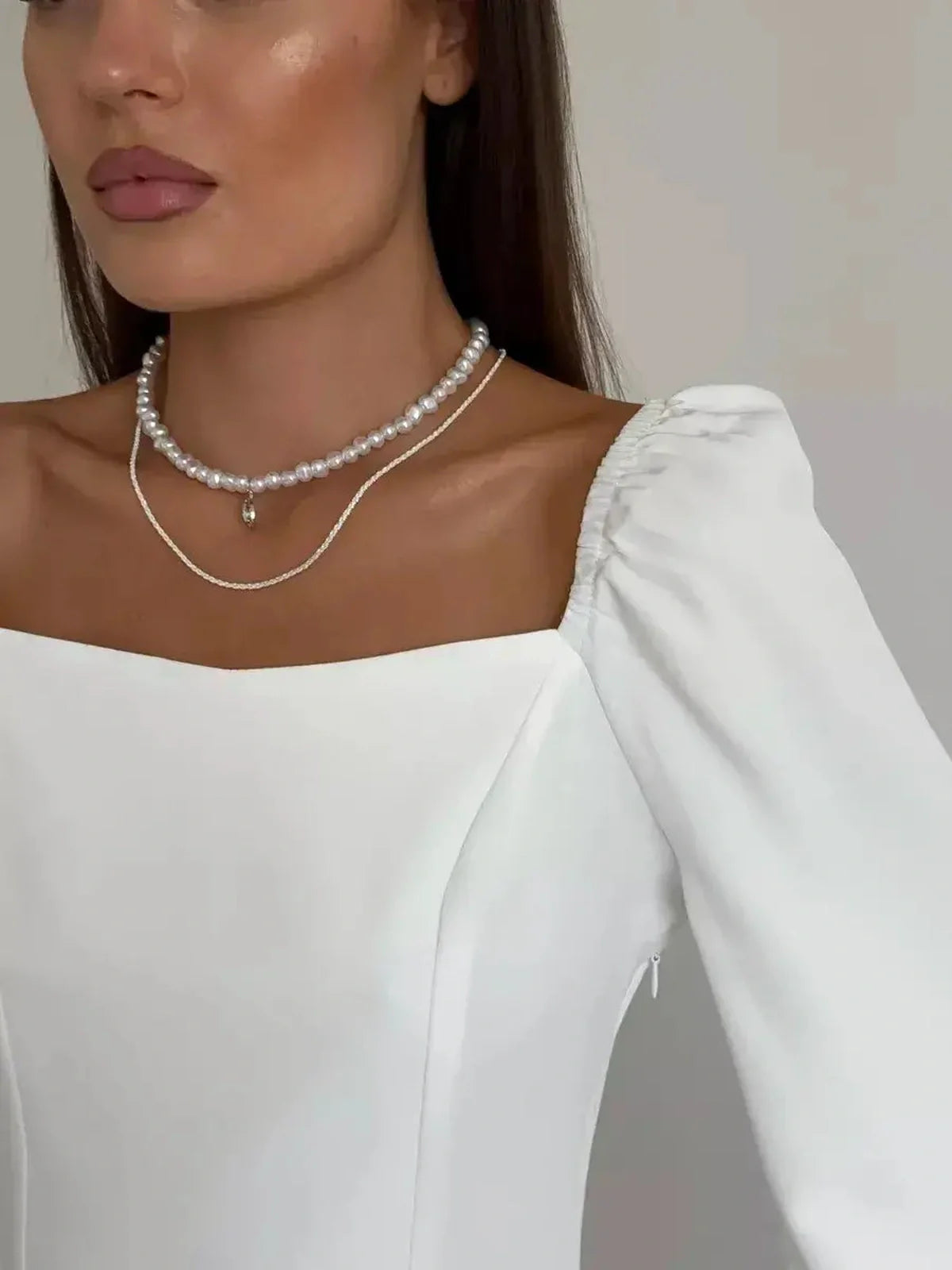 Close-up of a model in a sophisticated white dress with a square neckline and puffed sleeves, showcasing elegant jewelry.