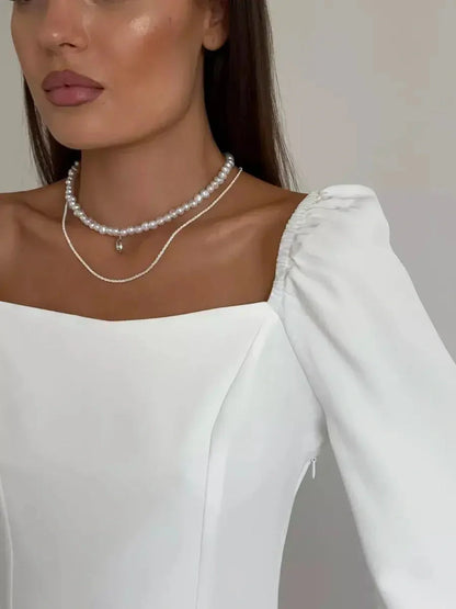 Close-up of a model in a sophisticated white dress with a square neckline and puffed sleeves, showcasing elegant jewelry.