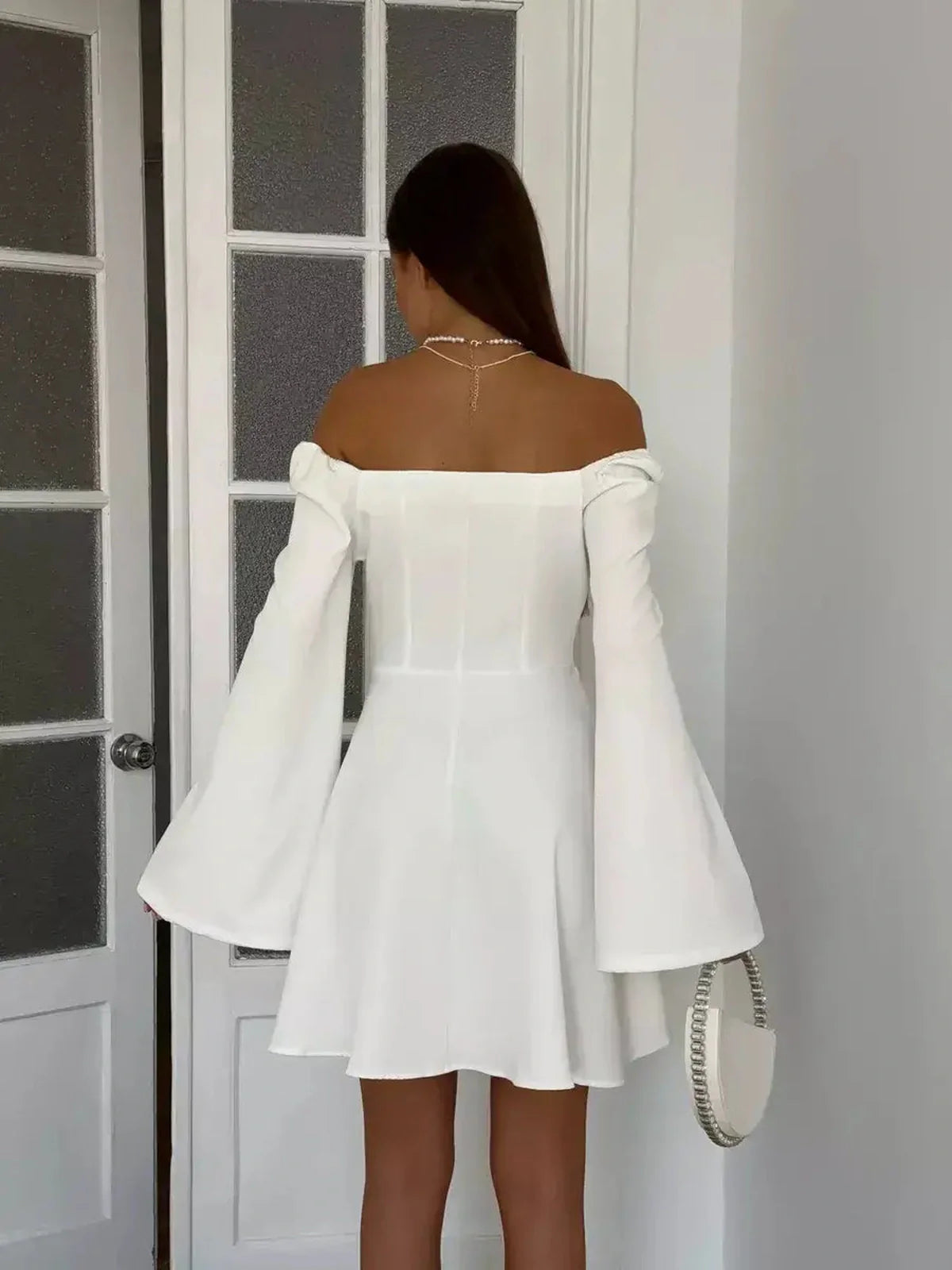 Back view of a woman in a white mini dress with flared sleeves, perfect for weddings or formal occasions.
