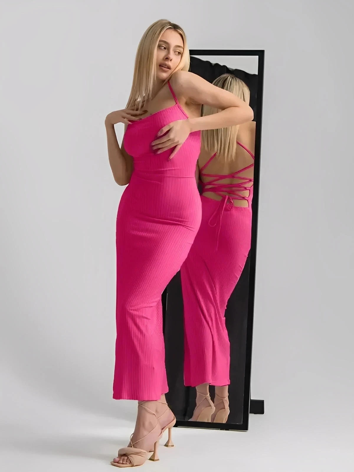 Model in a vibrant pink strappy knit midi dress with lace-up back detail, showcased in front of a mirror.