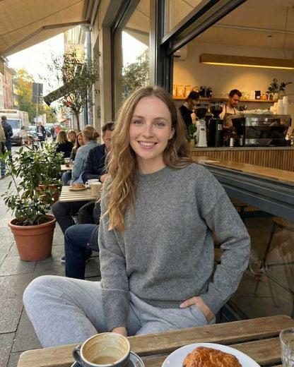 A woman wearing the Lyra Pullover by Lauven, enjoying coffee in a cozy café setting.