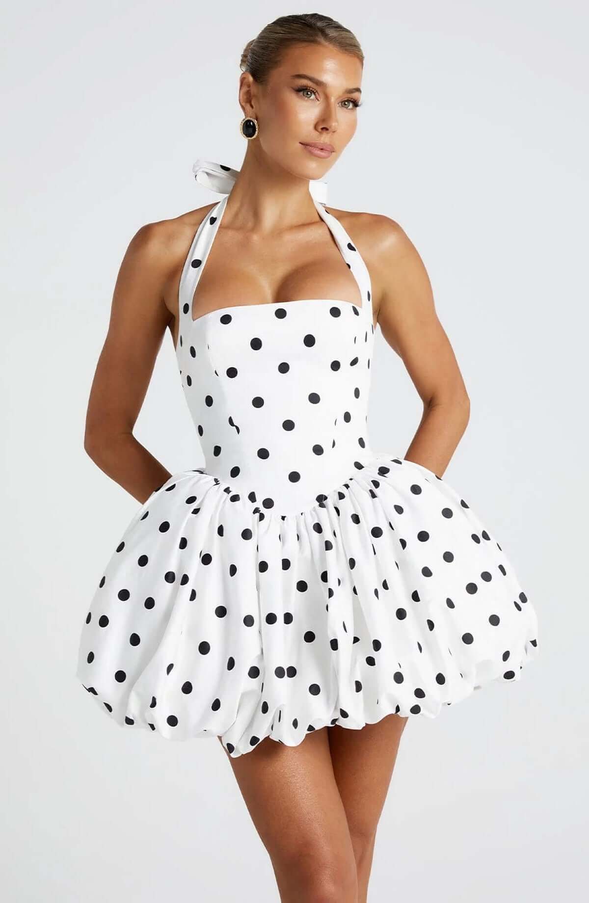 White mini dress with black polka dots and halter neckline, perfect for summer and a stylish addition to any wardrobe.