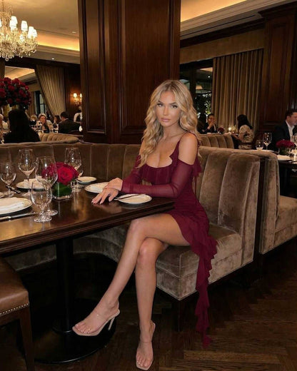 Elegant woman wearing Marina Mini Dress with ruffled asymmetric hem in burgundy at an upscale restaurant.