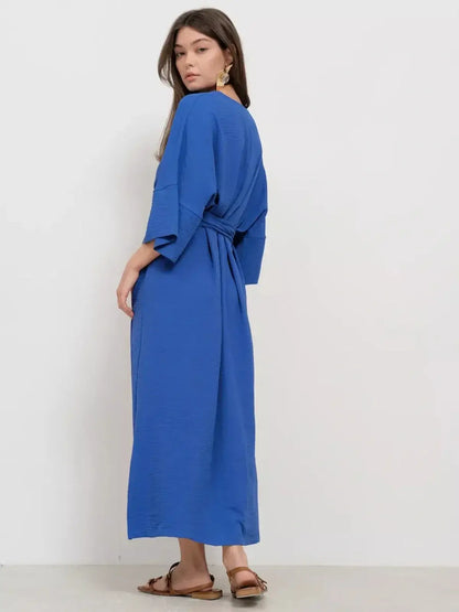 Model wearing Maxi Dress Azure Flow in blue, showcasing relaxed silhouette with tie-belt and deep V-neckline.