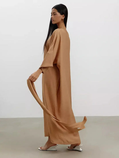 Model showcasing the Maxi Dress Dune Whisper in a sandstone hue, featuring wide sleeves and a flowing silhouette.