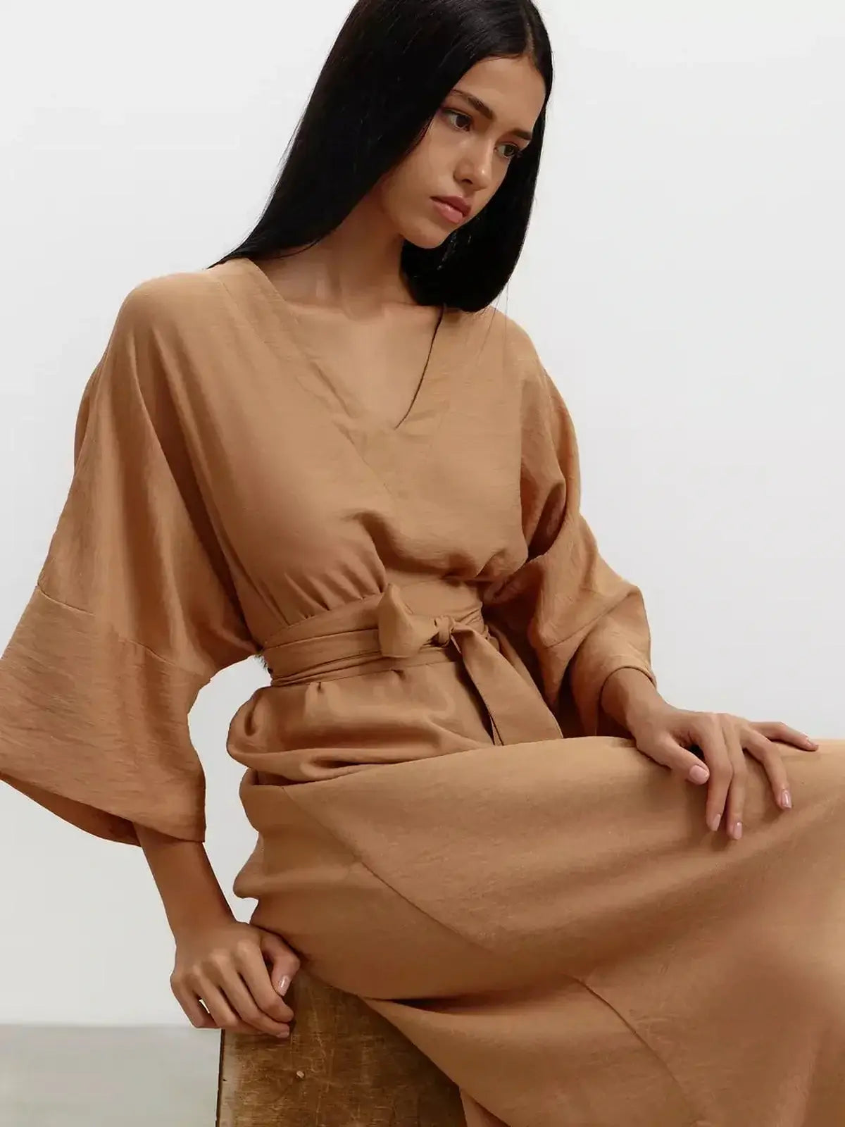 Model wearing a flowing maxi dress in sandstone hue, featuring wide kimono sleeves and a detachable tie belt.