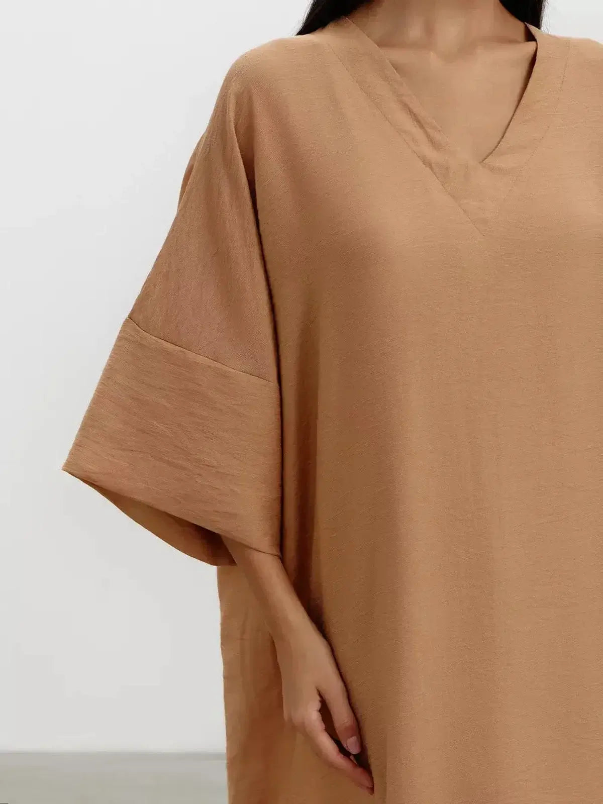 Close-up of a model wearing a V-neck maxi dress in a sandstone hue with wide kimono-style sleeves.
