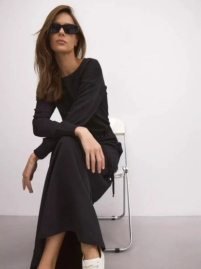 Model wearing a sleek black maxi dress with long sleeves and sunglasses, showcasing urban elegance and comfort.