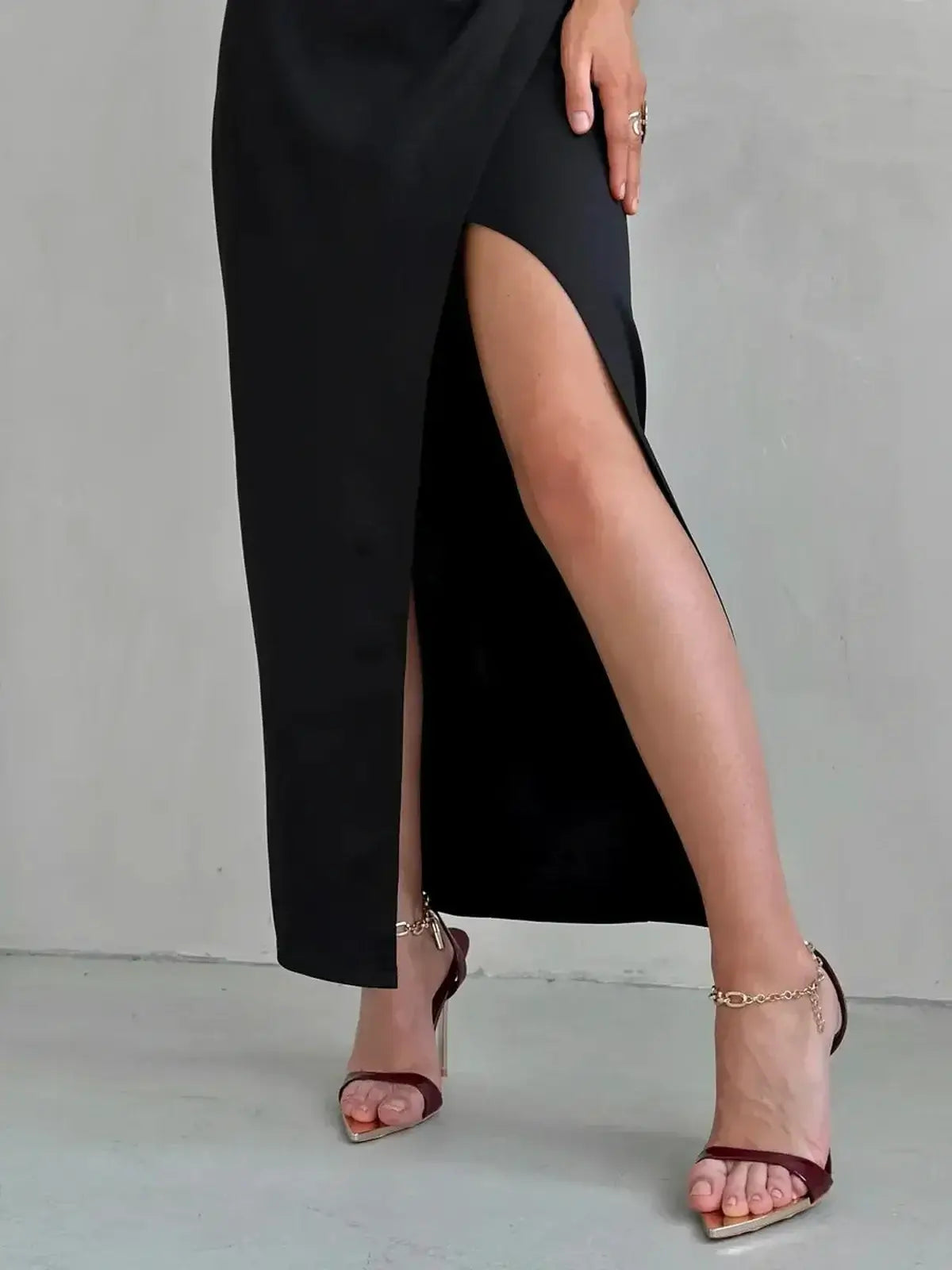 Model showcasing the leg slit of a black maxi dress, paired with elegant sandals, highlighting modern fashion.
