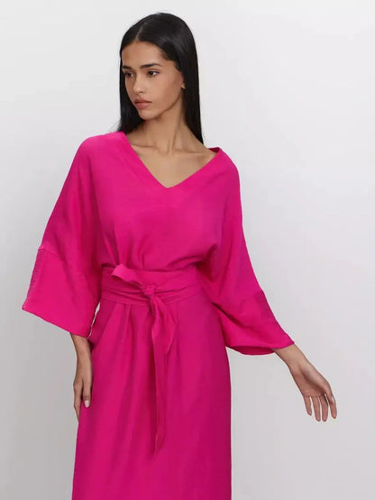 Model wearing a fuchsia maxi dress with a deep V-neck and kimono-style sleeves, highlighting its relaxed fit and removable belt.