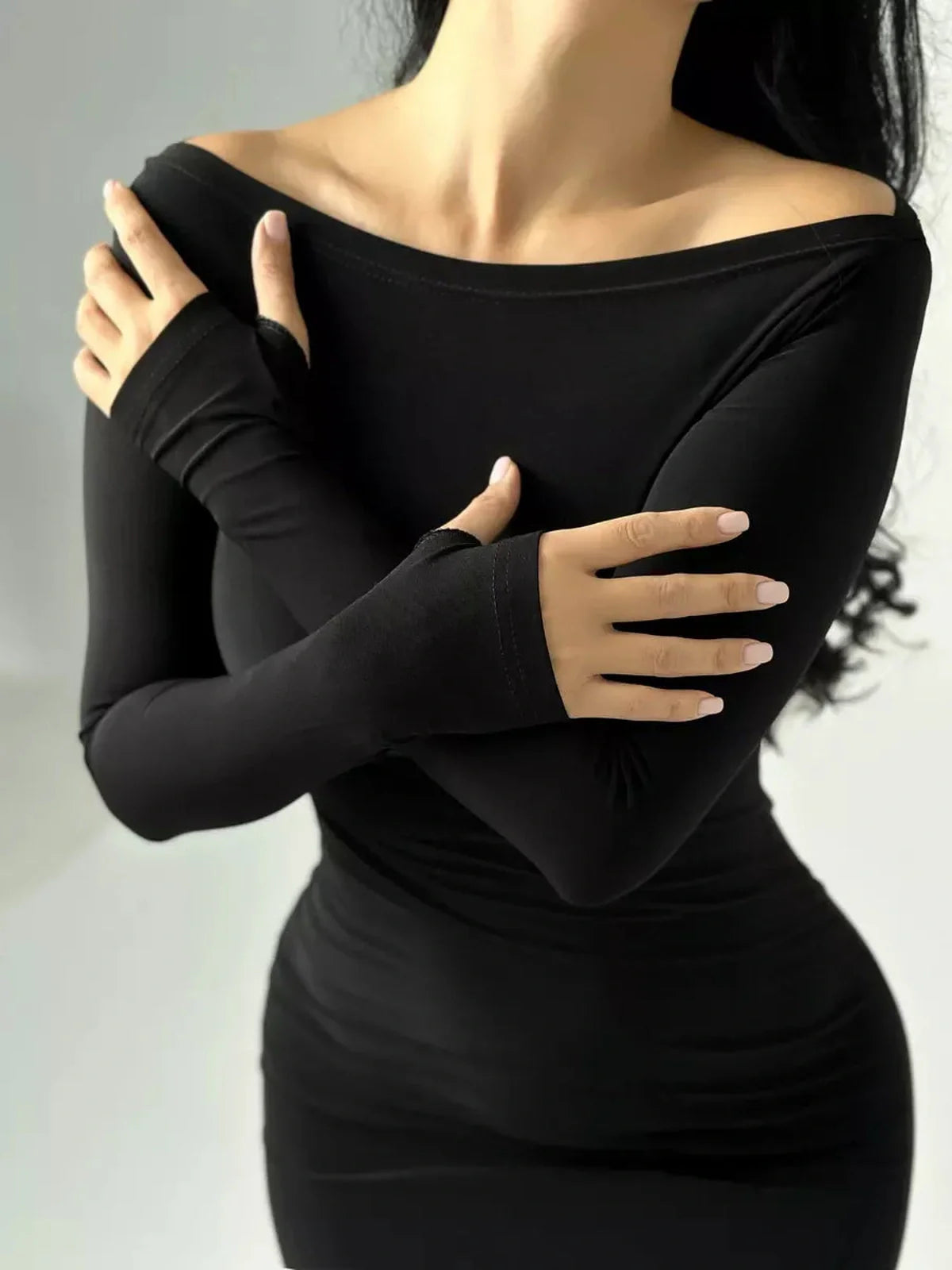 Elegant model wearing a black long sleeve bodycon maxi dress with thumbhole cuffs and modern boat neckline.