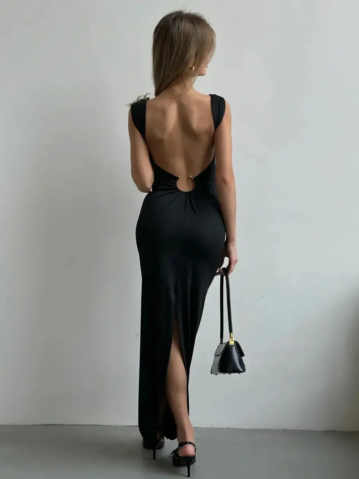 Rear view of a woman wearing the Maxi Dress Obsidian Charm, showcasing its plunging back and thigh-high slit.