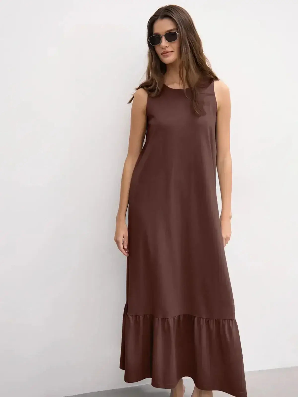Model wearing a chocolate-hued sleeveless maxi dress with a ruffle hem, perfect for chic and elegant off-duty style.