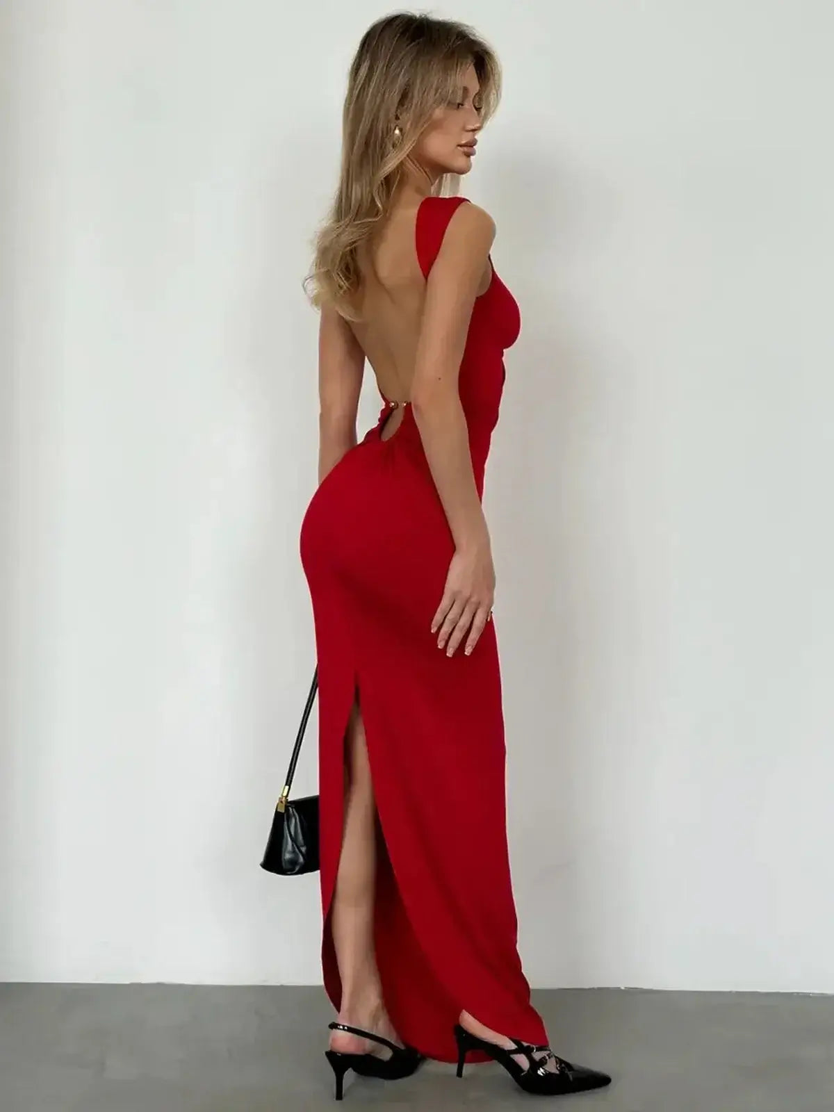 Back view of a woman in a red maxi dress with a sleek design and side slit, showcasing gold ring details and elegant silhouette.