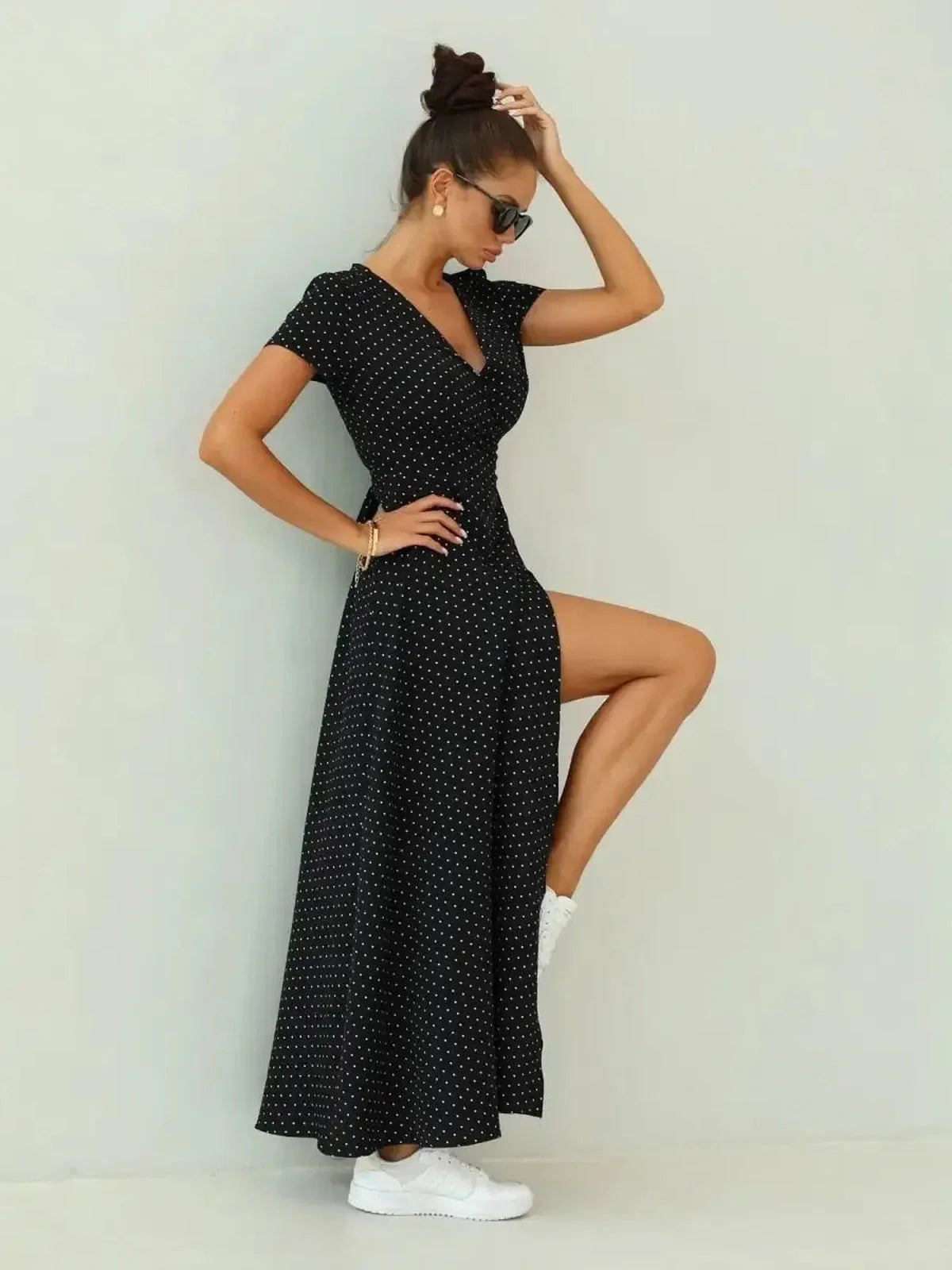 Elegant woman in Midnight Dots Maxi Dress with wrap silhouette, polka dots, and thigh-high slit, styled with white sneakers.
