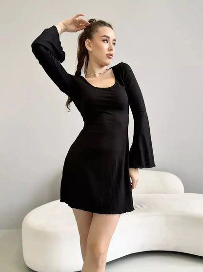 Model showcasing the Noir Flare black mini dress with flared sleeves and a deep square neckline.