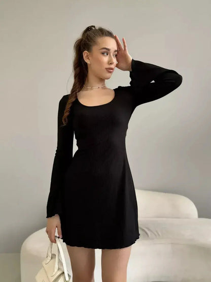 Stylish woman in a figure-enhancing black mini dress with flared long sleeves and a deep square neckline.