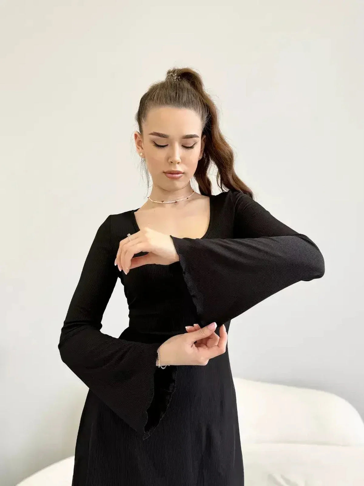 Model showcasing the Noir Flare black dress with flared sleeves and a deep square neckline.