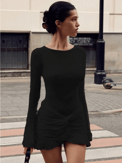 Model wearing a chic black mini dress with long sleeves and asymmetrical draping, perfect for evening wear.