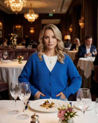 Nova Cardigan by Lauven worn by a woman in a restaurant setting, showcasing vibrant blue knitwear and elegant dining.