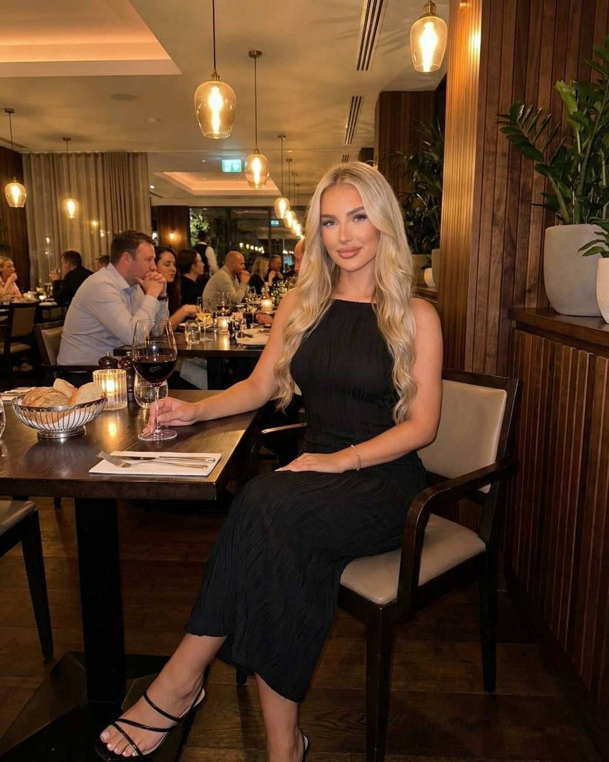 Elegant woman wearing the Nova Midi Dress at a restaurant, enjoying wine and ambient dining.