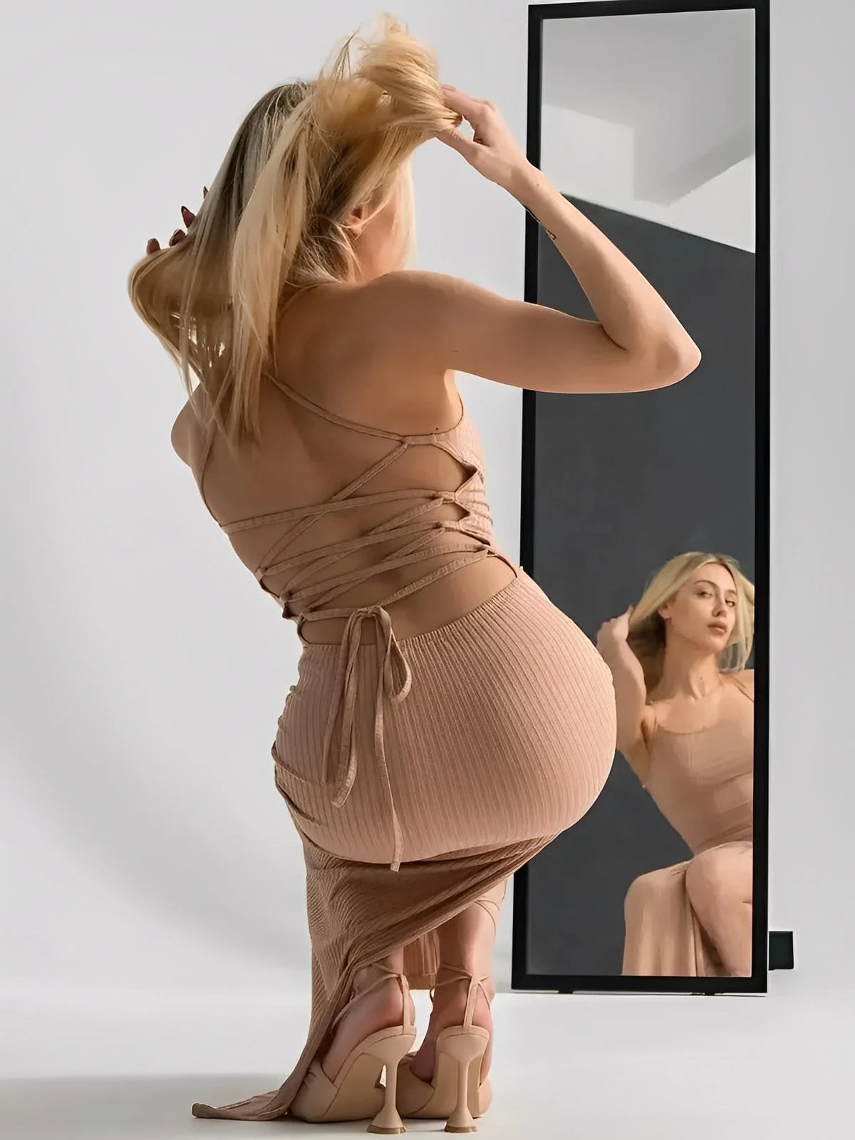 Nude lace midi dress with corset back, sculpting ribbed fit, showcasing thigh-high slit and adjustable straps in front of a mirror.