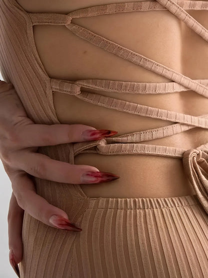 Close-up of a woman's hand adjusting the lace-up back of a nude lace midi dress featuring a ribbed design.