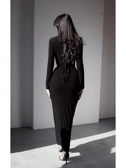 Back view of a woman in a sleek black Obsidian Drape Maxi Dress, showcasing its elegant silhouette and tie detail.