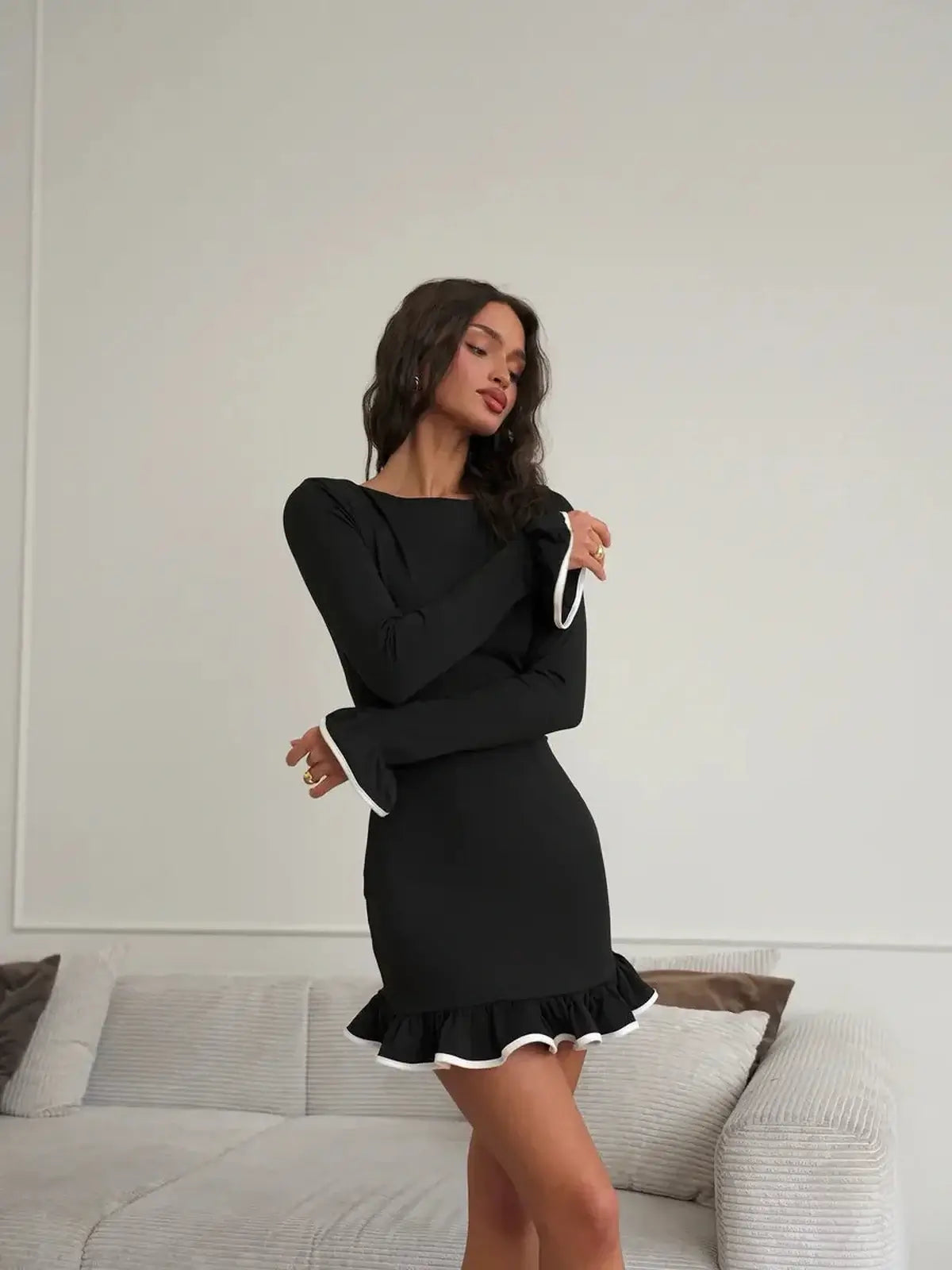 Model wearing a black long sleeve mini dress with white ruffle trim, showcasing an elegant and chic style.