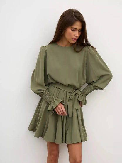 Olive Luxe Mini Dress features a round neckline, long sleeves, and a waist-cinching belt with feminine ruffles.