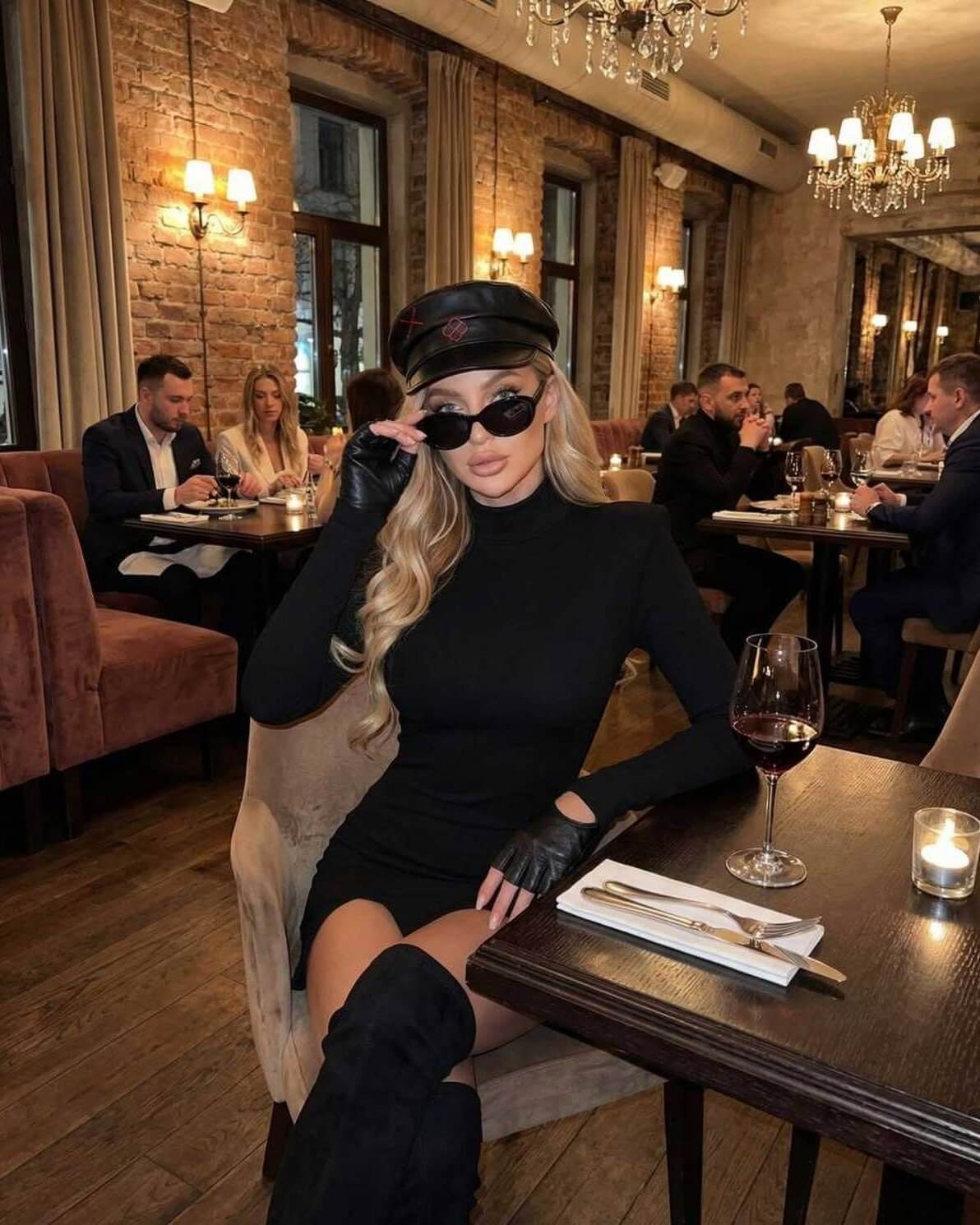 Orion Mini Dress worn by a woman in a stylish restaurant setting, showcasing its sleek black bodycon style.