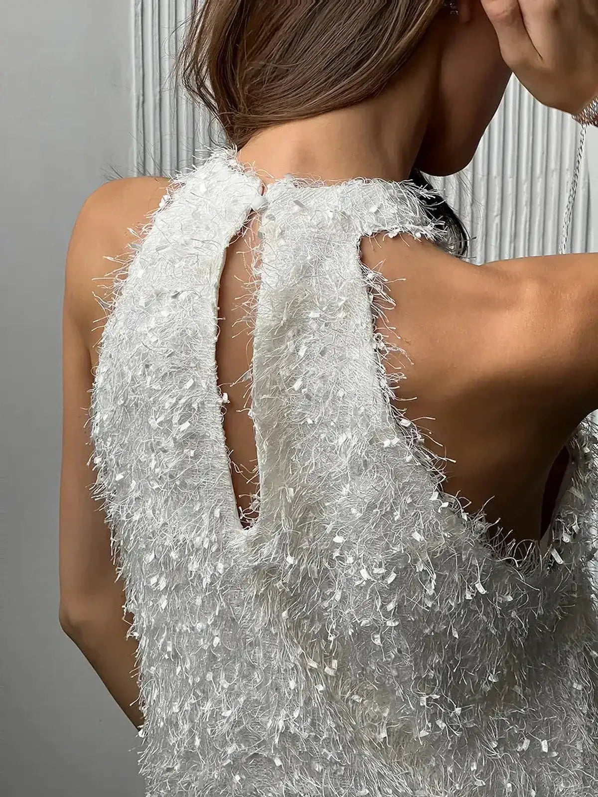 Close-up of the open back detail of a white pearl fringe mini dress, showcasing elegant texture and halter neckline.