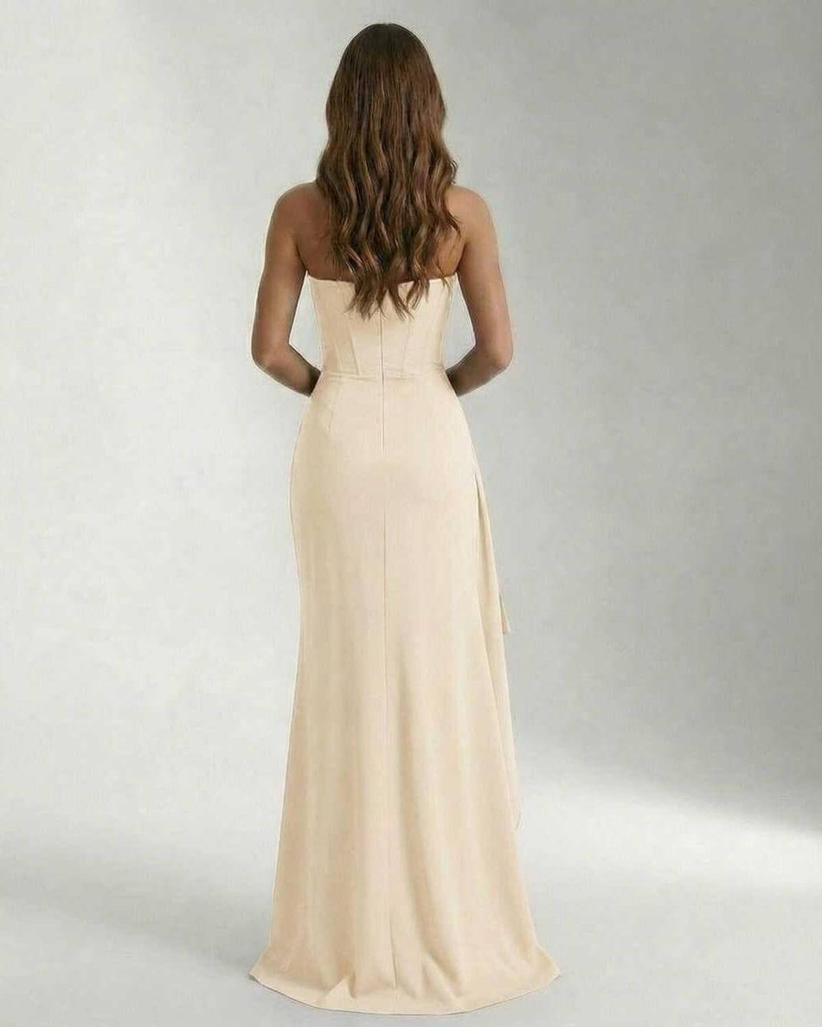 Back view of a woman in Lauven Marina Maxi Dress, showcasing the elegant strapless design and flowing beige fabric.