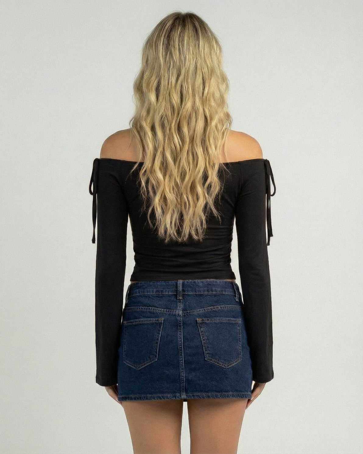 Back view of a woman wearing the Lauven Monaco Top, an off-the-shoulder long sleeve slim fit top, styled with a denim skirt.