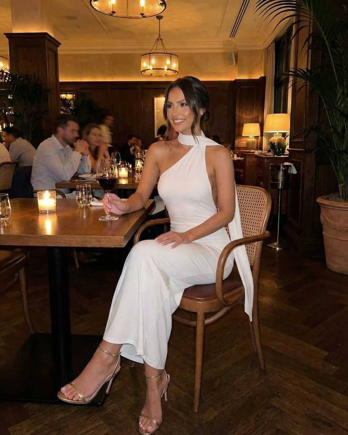 Model wearing the Luna Maxi Dress by Lauven, an elegant white halter neck gown, seated at a stylish dining table.