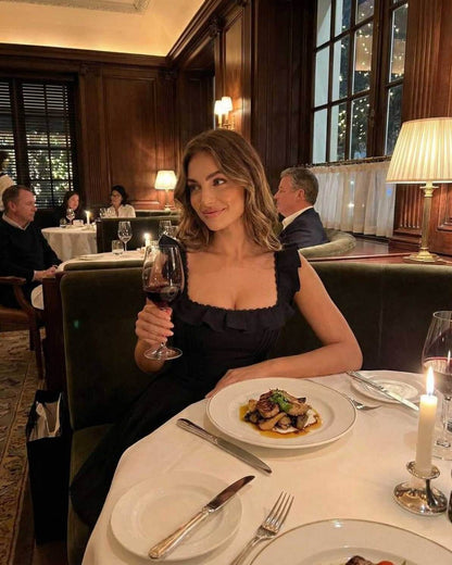 Serena Mini Dress by Lauven, a sleek black cotton blend dress with ruffle details, worn elegantly at a fine dining setting.