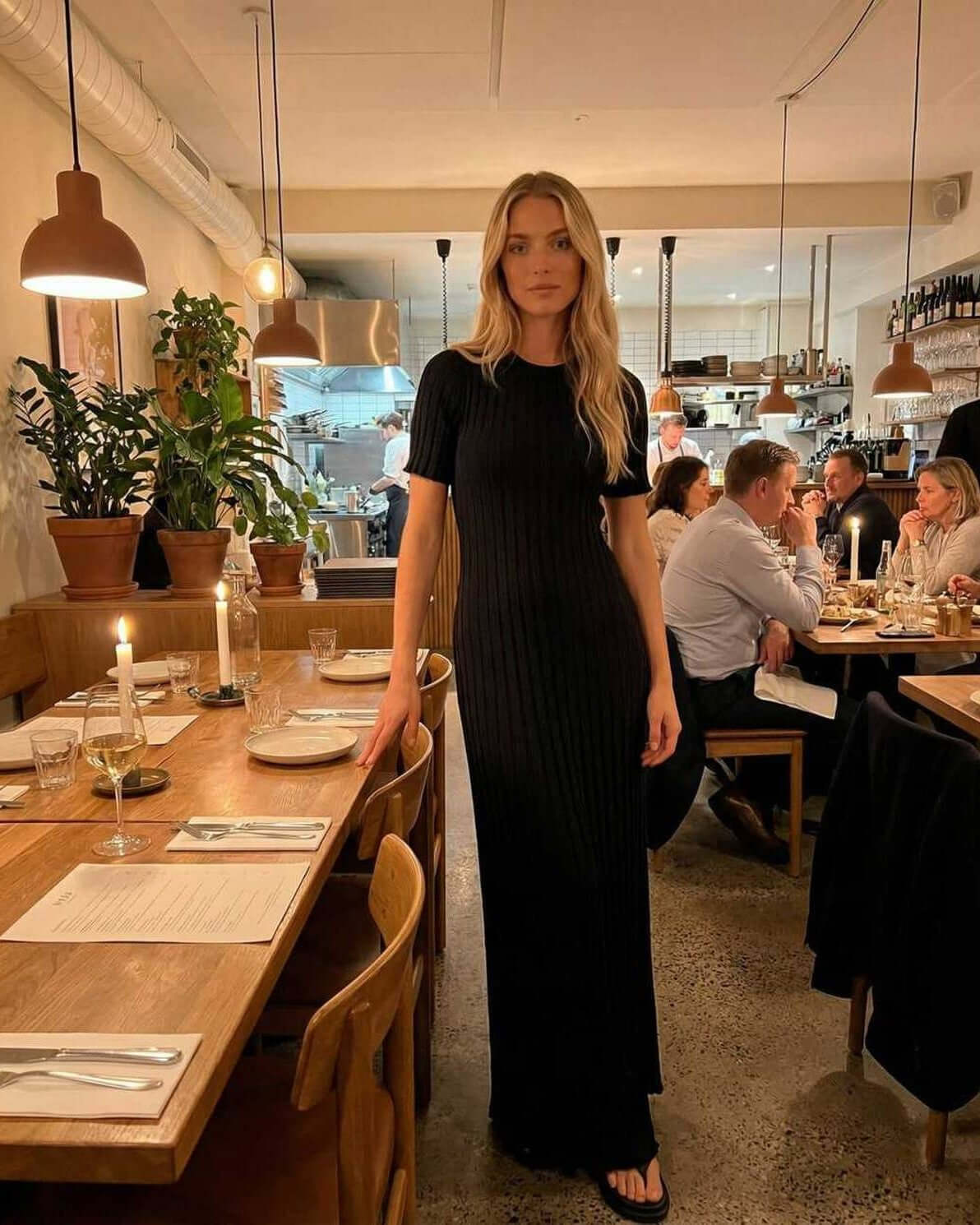 Luna Maxi Dress by Lauven worn by a model in a chic restaurant setting showcasing its elegant black ribbed knit design.