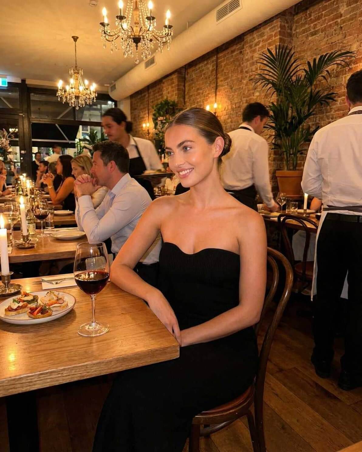 Elegant woman wearing the Noir Maxi Dress by Lauven, seated at a candlelit table in a sophisticated restaurant.