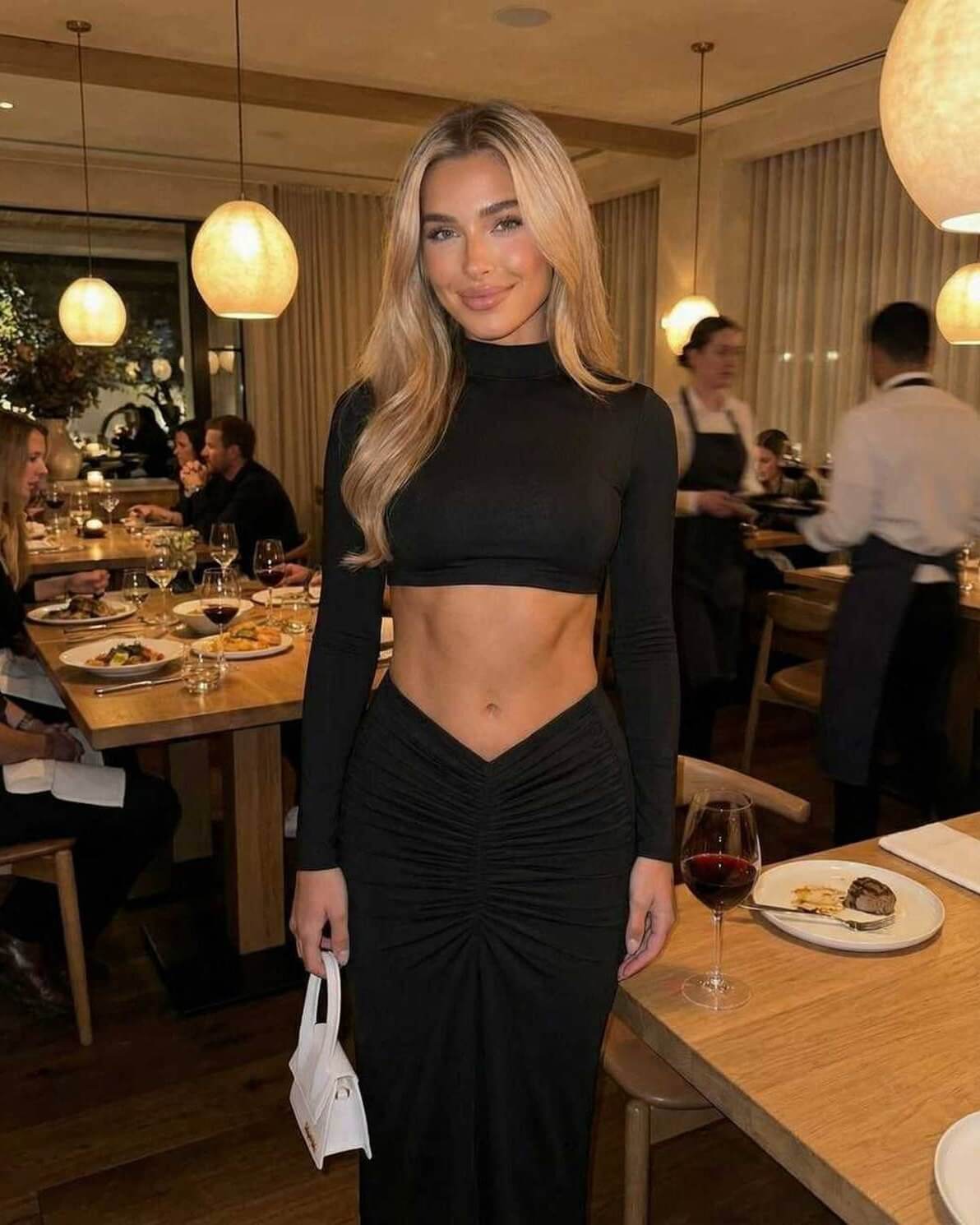 Noir Maxi Dress worn by a model in a restaurant setting, featuring elegant black fabric and flattering ruching.